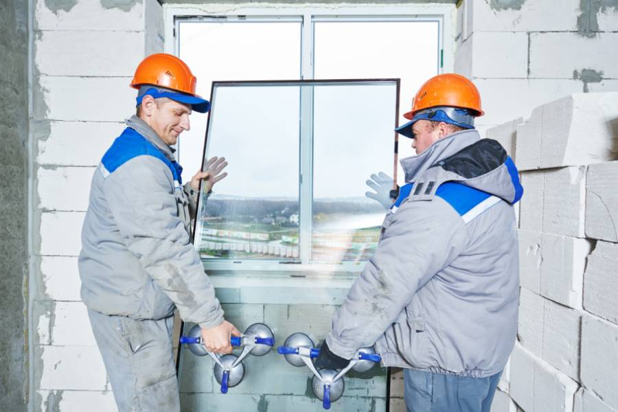 zwei Männer in Arbeits- und Schutzkleidung bringen eine Glasscheibe in die Fensterfassung ein